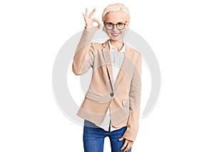 Young blonde woman wearing business clothes and glasses smiling positive doing ok sign with hand and fingers