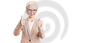 Young blonde woman wearing business clothes and glasses success sign doing positive gesture with hand, thumbs up smiling and happy