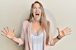 Young blonde woman wearing business jacket and glasses crazy and mad shouting and yelling with aggressive expression and arms