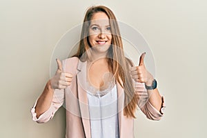 Young blonde woman wearing business jacket and glasses success sign doing positive gesture with hand, thumbs up smiling and happy