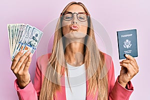 Young blonde woman wearing business style holding dollars and usa passport looking at the camera blowing a kiss being lovely and