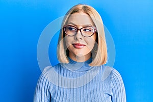 Young blonde woman wearing casual clothes and glasses smiling looking to the side and staring away thinking