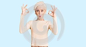 Young blonde woman wearing casual clothes looking surprised and shocked doing ok approval symbol with fingers