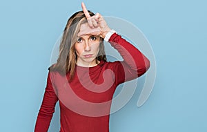 Young blonde woman wearing casual clothes making fun of people with fingers on forehead doing loser gesture mocking and insulting