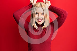 Young blonde woman wearing casual clothes posing funny and crazy with fingers on head as bunny ears, smiling cheerful