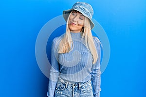 Young blonde woman wearing casual denim hat smiling looking to the side and staring away thinking