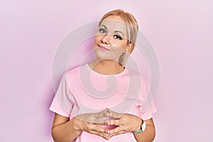 Young blonde woman wearing casual pink t shirt hands together and fingers crossed smiling relaxed and cheerful
