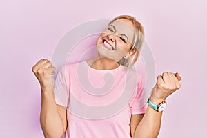 Young blonde woman wearing casual pink t shirt very happy and excited doing winner gesture with arms raised, smiling and screaming