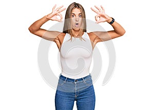Young blonde woman wearing casual style with sleeveless shirt looking surprised and shocked doing ok approval symbol with fingers