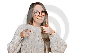 Young blonde woman wearing casual sweater and glasses pointing fingers to camera with happy and funny face