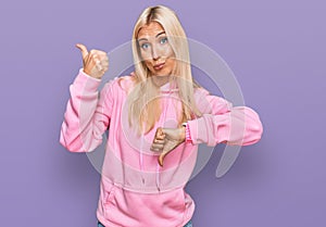 Young blonde woman wearing casual sweatshirt doing thumbs up and down, disagreement and agreement expression