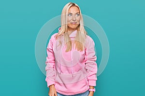 Young blonde woman wearing casual sweatshirt smiling looking to the side and staring away thinking