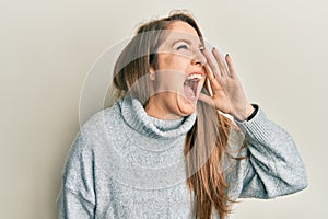 Young blonde woman wearing casual turtleneck sweater shouting and screaming loud to side with hand on mouth