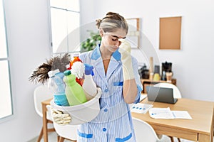 Young blonde woman wearing cleaner uniform holding cleaning products tired rubbing nose and eyes feeling fatigue and headache