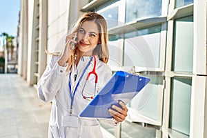 Young blonde woman wearing doctor uniform talking on the smartphone at hospital