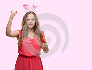 Young blonde woman wearing easter bunny ears annoyed and frustrated shouting with anger, crazy and yelling with raised hand, anger