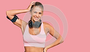 Young blonde woman wearing gym clothes and using headphones confuse and wonder about question