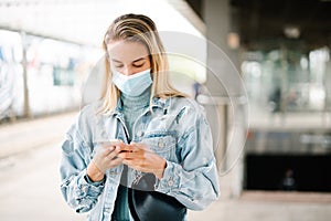 Young blonde woman wearing mask waiting in a bus station