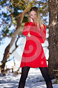 Young blonde woman wearing a red dress and black stockings in the snowy mountains in winter.