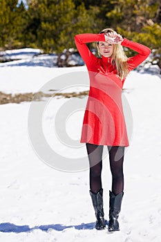 Young blonde woman wearing a red dress and black stockings in the snowy mountains in winter.