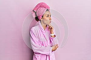 Young blonde woman wearing shower towel cap and bathrobe thinking worried about a question, concerned and nervous with hand on