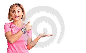 Young blonde woman wearing sportswear showing palm hand and doing ok gesture with thumbs up, smiling happy and cheerful