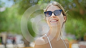 Young blonde woman wearing sunglasses looking to the sky smiling at park