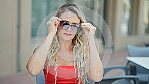 Young blonde woman wearing sunglasses sitting on table at coffee shop terrace