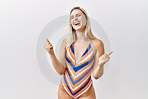 Young blonde woman wearing swimsuit over isolated background very happy and excited doing winner gesture with arms raised, smiling