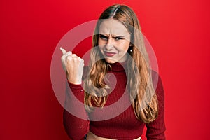 Young blonde woman wearing turtleneck sweater angry and mad raising fist frustrated and furious while shouting with anger