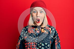 Young blonde woman wearing wool winter cap scared and amazed with open mouth for surprise, disbelief face