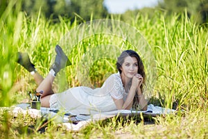 Young blonde woman in white dress lies on a picnic sheet in tall grass