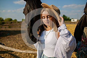 Young Blonde Woman In White Shirt Stroking A Brown Horse In Summer Countryside.