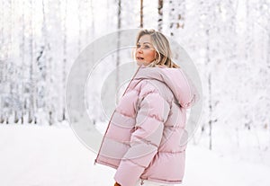 Young blonde woman in winter clothes walking in snowy winter forest