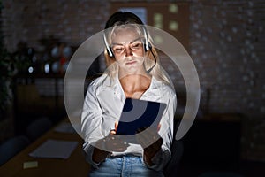 Young blonde woman working at the office at night looking sleepy and tired, exhausted for fatigue and hangover, lazy eyes in the