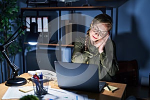 Young blonde woman working at the office at night sleeping tired dreaming and posing with hands together while smiling with closed