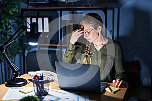 Young blonde woman working at the office at night tired rubbing nose and eyes feeling fatigue and headache