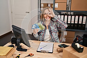 Young blonde woman working at small business ecommerce holding chilean pesos banknotes smiling happy doing ok sign with hand on