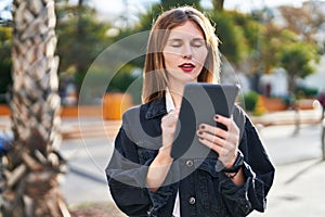 Young blonde woman writing on touchpad with serious face at park