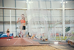 Young blonde women performing a long jump in the sports arena