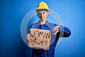 Young blonde worker woman asking for women rights holding banner with power message with angry face, negative sign showing dislike