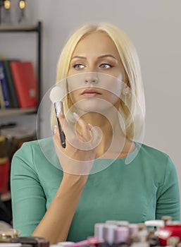 A young blonde 25-30 years old puts makeup on her face, close-up, selective focus.