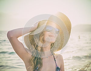 Young blondy girl in sunglasses and straw hat at the beach