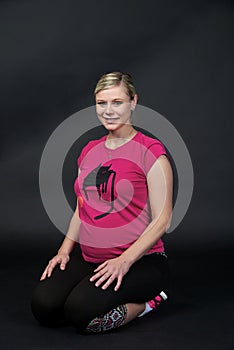 Young blondy pregnant woman in pink t-short with cat on black background.