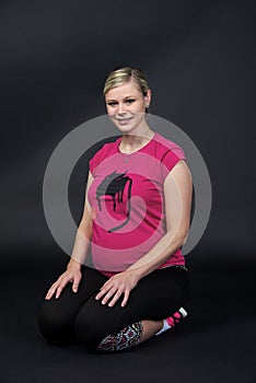 Young blondy pregnant woman in pink t-short with cat on black background.