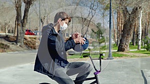 A young bmx rider in medical mask sitting on a bike and wearing a helmet