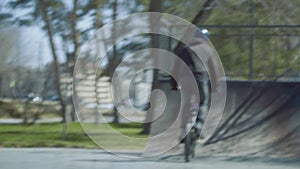 A young bmx rider rides on ramp and does an ollie tricks in the skatepark