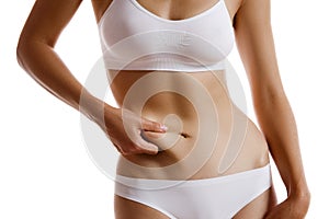 Young body of girl in white underwear, showing fat on her belly, posing isolated on white. Plastic surgery, aesthetic