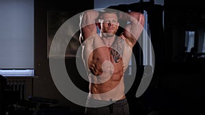Young bodybuilder with a bare torso posing in a gym. 60 to 24fps 4K