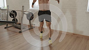 Young bodybuilder naked torso spreads a mat to the floor for a gym training and turns on a sports timer on a mobile